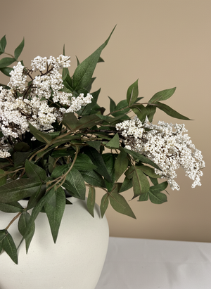 Faux white berry clusters with green foliage arranged in a matte white ceramic vase against a neutral background #white