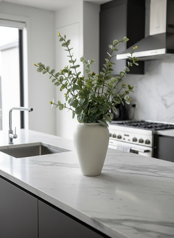 Premium faux eucalyptus arrangement with soft green foliage styled in a matte ceramic vase on a marble kitchen island 
