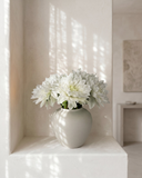 Real touch white faux dahlia arrangement in a matte ceramic vase on a concrete shelf in a softly lit room #white