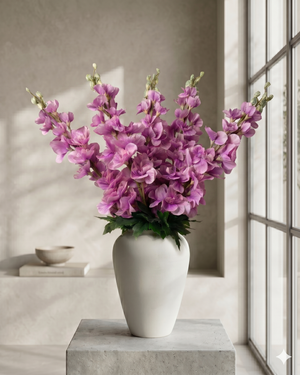 Realistic faux pink delphinium stems arranged in a white ceramic vase on concrete surface against a warm neutral backdrop #lavender-pink