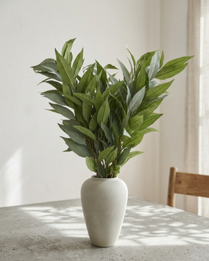 Real touch faux eucalyptus stems arranged in neutral ceramic vase on marble table