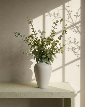 White vase with eucalyptus stems on a light surface with a neutral background