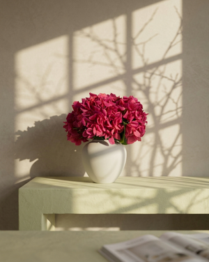 White vase with pink hydrangea flowers on a surface with sunlight casting shadows. #fuchsia-pink