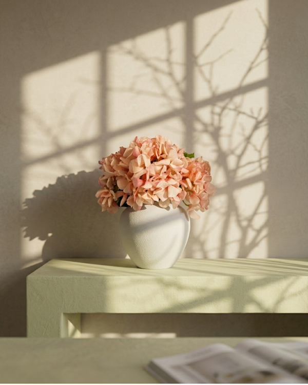 Pink hydrangea flowers in a white vase on a light surface with shadows from branches on the wall. #peachy-pink