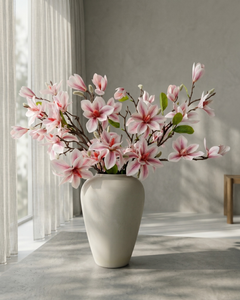 Pink faux magnolia blossom arrangement in large beige vase on concrete table, luxury artificial spring floral decor