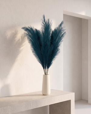 White vase with premium teal faux pampas grass on a concrete surface against #deep-teal 
