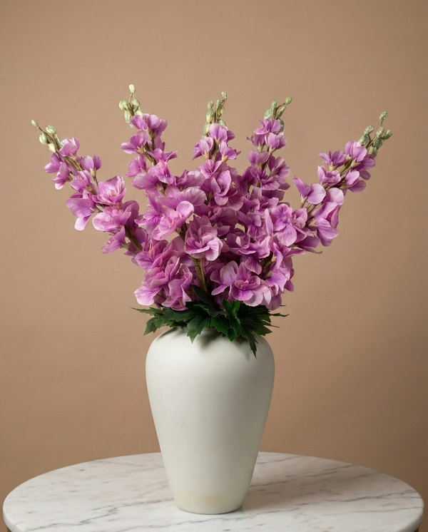 Realistic faux pink delphinium stems arranged in a white ceramic vase against a warm neutral backdrop #lavender-pink