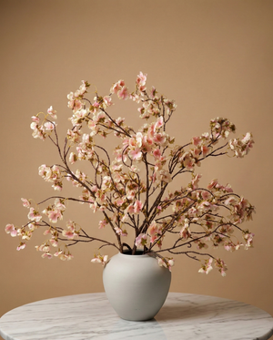 Lifelike faux blush pink cherry blossom branches in a white ceramic vase on a marble table with a tan background #blush-pink