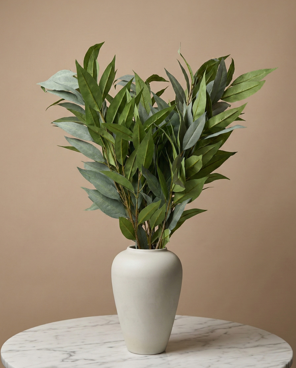 Real touch faux eucalyptus stems arranged in neutral ceramic vase on marble table