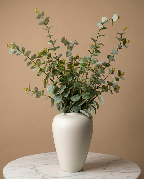 Real touch faux eucalyptus stems with soft green foliage styled in a matte ceramic vase on a marble table 