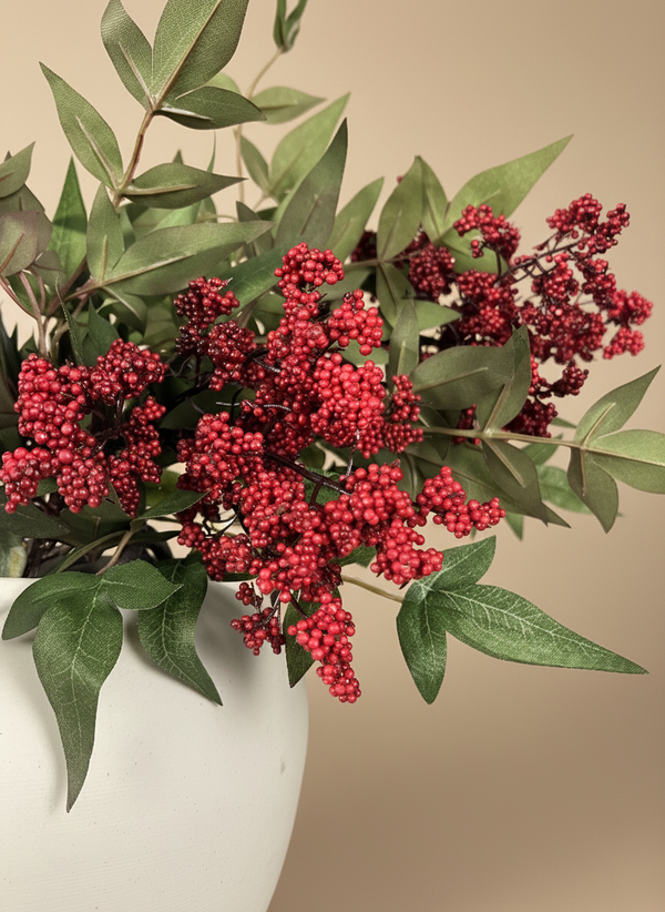 Faux red berry clusters with green foliage arranged in a matte white ceramic vase against a neutral background #red