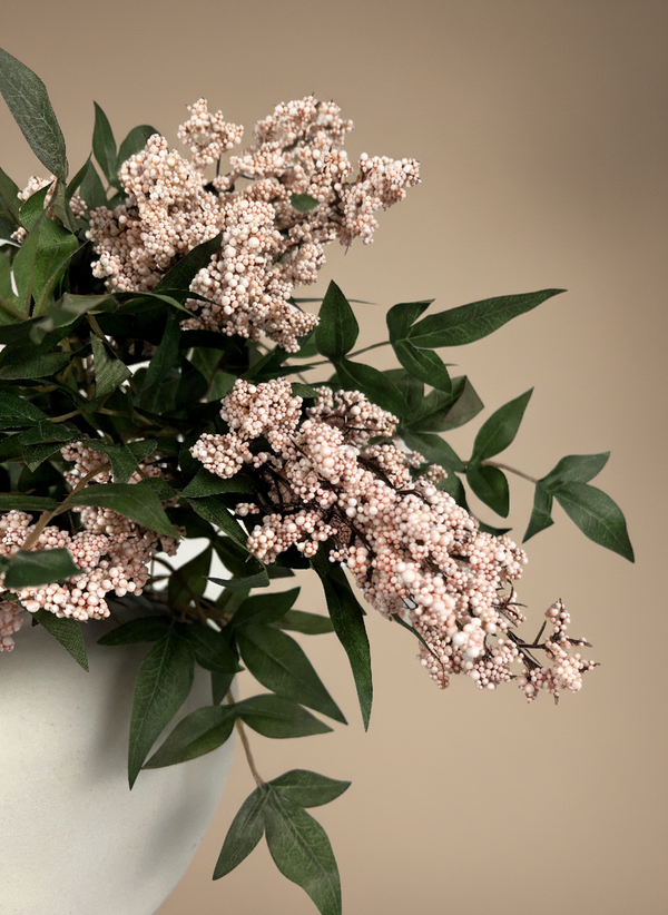 Faux pink berry clusters with green foliage arranged in a matte white ceramic vase against a neutral background #pale-pink