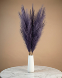 White vase with dried faux violet pampas grass on a marble surface against a beige background #deep-violet