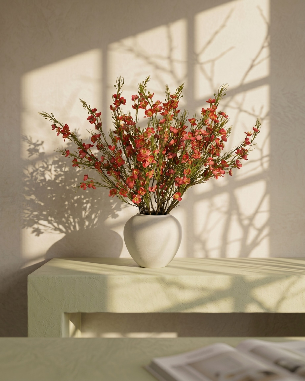 Matte white vase with real touch faux red wax flower arrangement with delicate blooms on a light surface with a soft shadow background #red