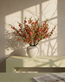 Matte white vase with real touch faux red wax flower arrangement with delicate blooms on a light surface with a soft shadow background #red