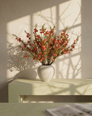 Matte white vase with real touch faux red wax flower arrangement with delicate blooms on a light surface with a soft shadow background #red