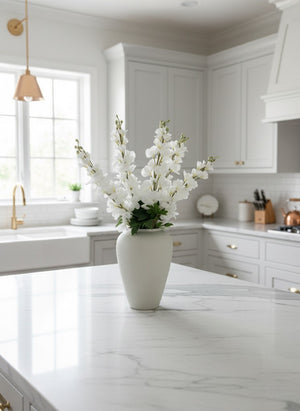 Realistic faux white delphinium flowers arranged in a white matte vase on a bright, modern kitchen island #white