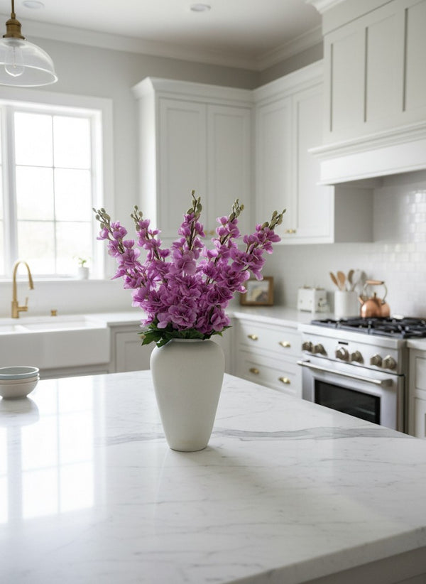 Realistic faux pink delphinium flowers arranged in a white matte vase on a bright, modern kitchen island #lavender-pink